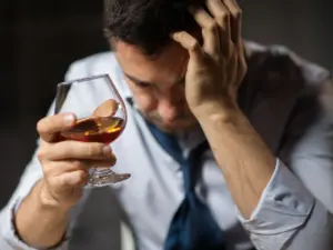 Man experiencing alcohol cravings and emotional distress while holding a glass of alcohol