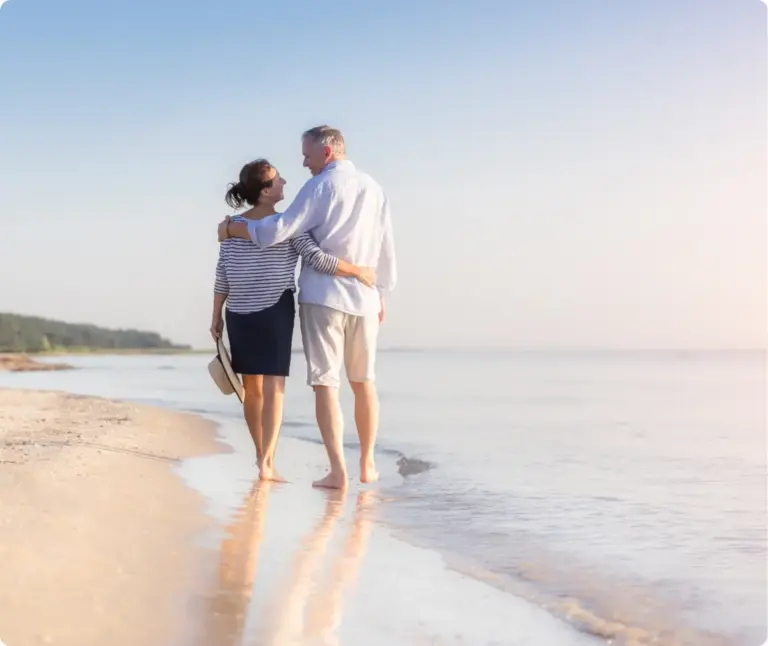 Mature couple walking barefoot along the beach, representing healing, recovery, and long-term sobriety after addiction treatment.